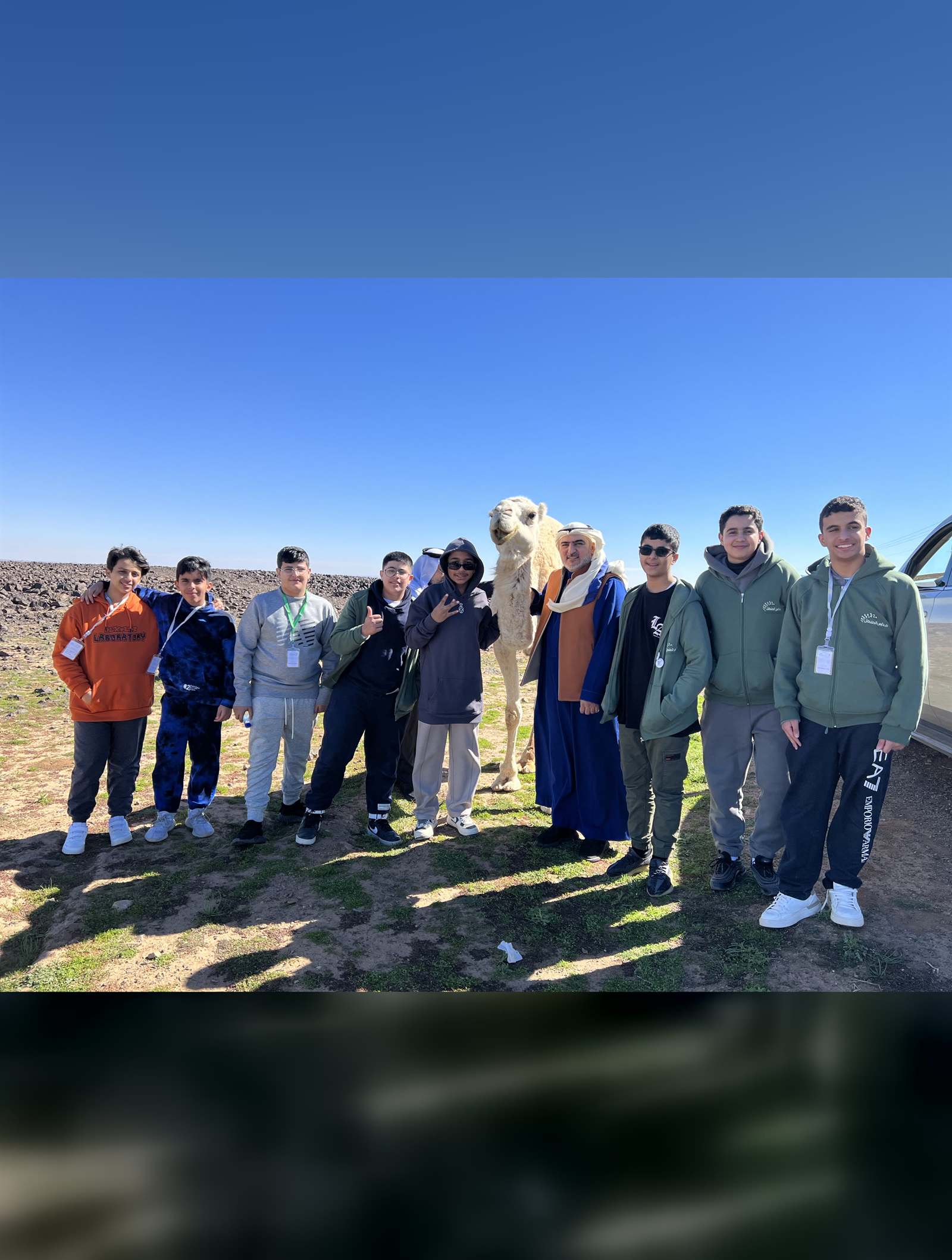 A student group beside a camel in AlUla under clear sky