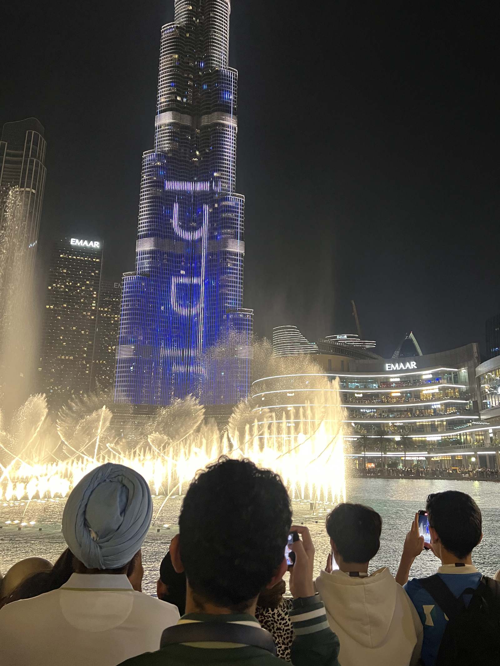 The Dubai Fountain before Burj Khalifa at night, spectators seen from behind